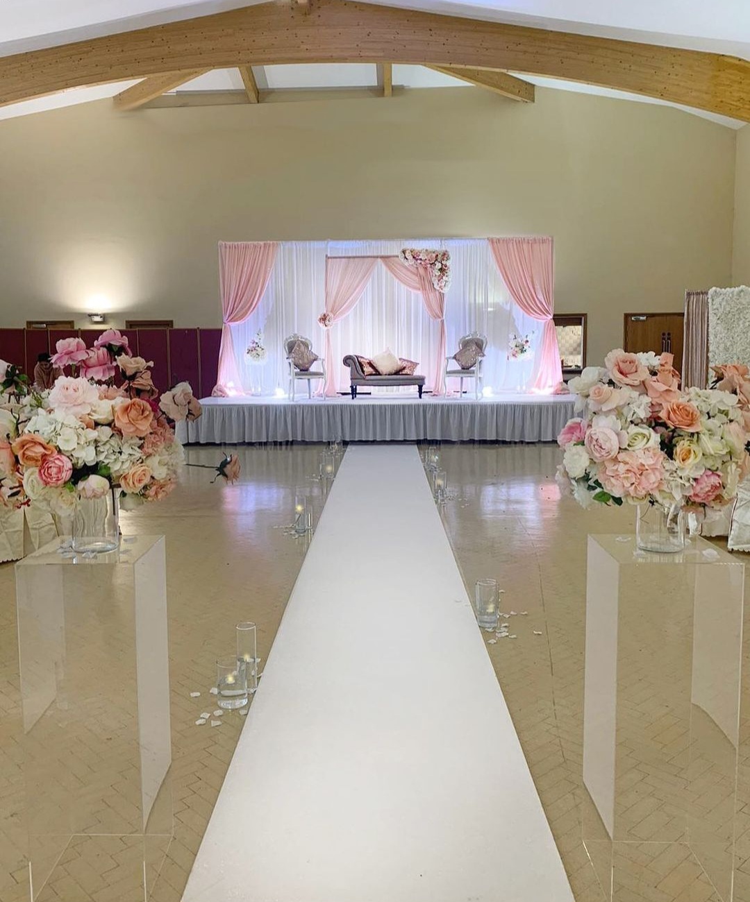 Wedding stage setup with pink drapes and floral aisle in the community centre